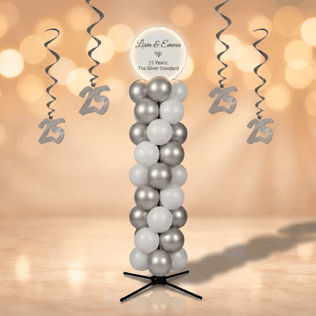 Silver and white balloon column with round white top board featuring anniversary names, standing in a champagne-gold ballroom with crystal chandeliers