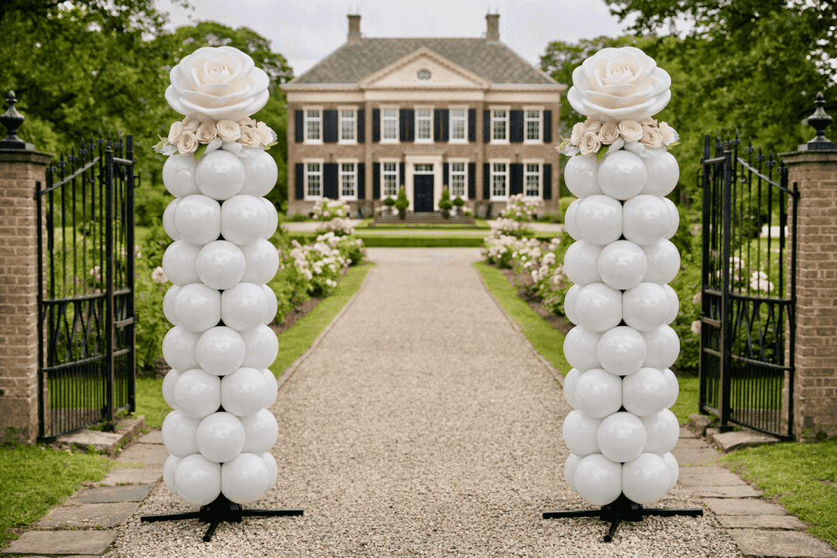 Two white balloon pillars with pink flowers at a manor entrance